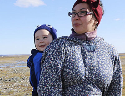 A woman wearing glasses and a red hat holds a baby in a blue jacket.