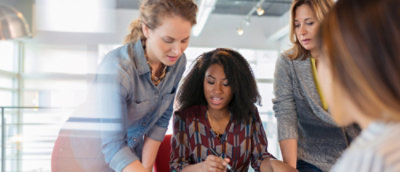 Three women share insights and review documents in a shared office workspace.
