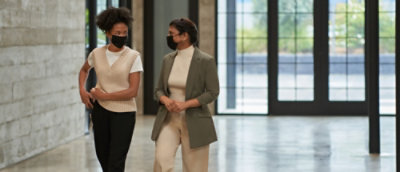 Two masked women walk through an office, highlighting safety protocols.