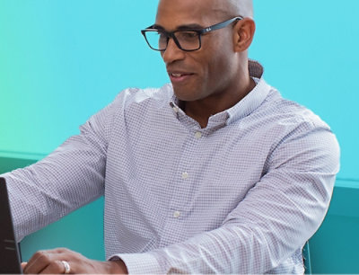 A man wearing glasses and a button-up shirt sitting in a chair.