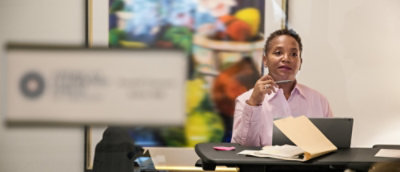 Detailní pohled na stůl se složkou a rozmazanou obrazovkou počítače na pozadí.