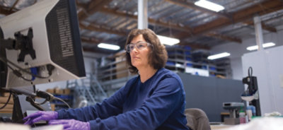 A woman wearing safety glasses and working on a computer.