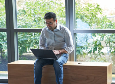 A man sitting on a window sill using a laptop.