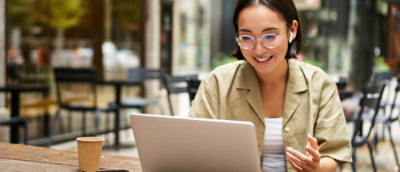 A woman wearing glasses and smiling at a laptop.