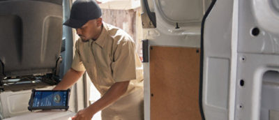 A man operates a tablet to open a van door, standing beside the vehicle.