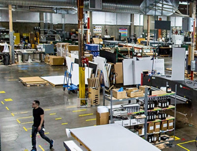 A man walking in a warehouse with shelves of bottles and boxes visible.