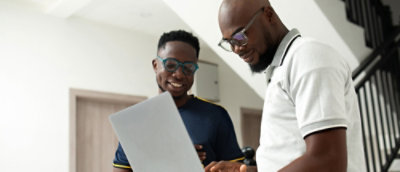 A man wearing glasses and smiling while looking at a laptop.