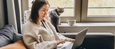 A person sitting in front of a laptop with a cat in the background.