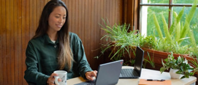 A person using a laptop at a table with a cup of coffee and a potted plant nearby.