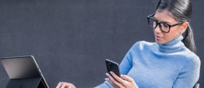A woman wearing glasses and a blue turtleneck holding a phone.