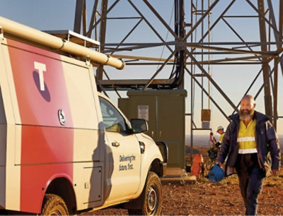 A man in a yellow shirt and blue jacket walking next to a white and red van with a red stripe.