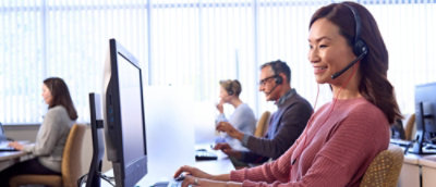 A group of people sitting at desks and working on computers, with some wearing headsets.