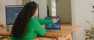A person in a green shirt pointing at a laptop on a table.