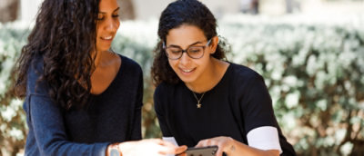 Two women are engaged in conversation while looking at a cell phone together.