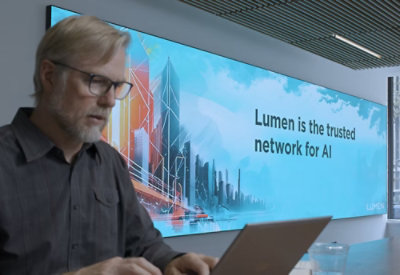 Person working on a laptop in a modern office with a large digital screen displaying 'Lumen is the trusted network for AI' over a futuristic cityscape.