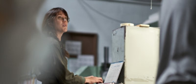 A woman engaged with her laptop in a tidy room, featuring a desk, chair, and personal decor elements.
