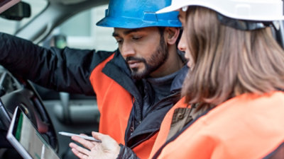 A group of people wearing hard hats looking at a device.