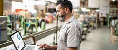 A man using a laptop in a factory setting.