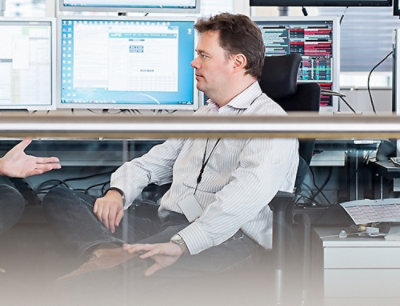 Personne en chemise rayée assise sur une chaise de bureau, plusieurs écrans derrière