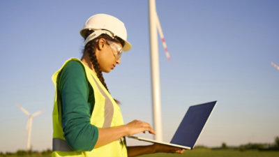 Une personne portant un casque blanc et un gilet de sécurité jaune utilise un ordinateur portable.
