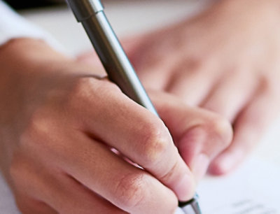 A close-up of a person's hands holding a pen over a piece of paper.