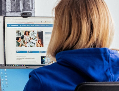 A person in a blue hoodie sits at a desk, focused on a computer screen displaying an educational website.