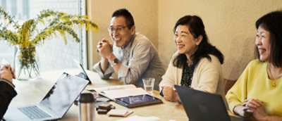 A man and woman sitting at a table with a laptop and a potted plant.