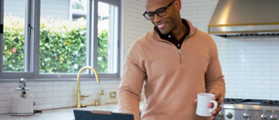 A man holding a cup and looking at a laptop.