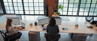 A woman sitting at a desk with two computers.