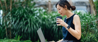 A person holding a coffee cup and looking at a laptop.