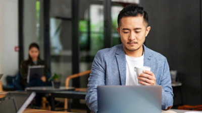 A man holding a cup and looking at a laptop.