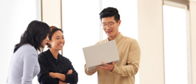 A person holding a laptop next to another person with crossed arms.