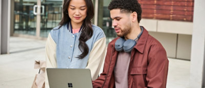 A man and woman sit outside with a laptop.