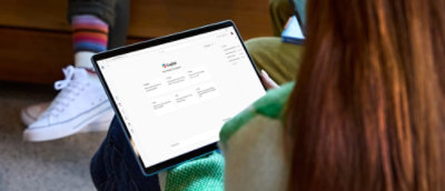 A person in a green sweater holds a tablet displaying a Copilot app.