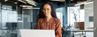 A woman at desk working on a laptop in a bright office.