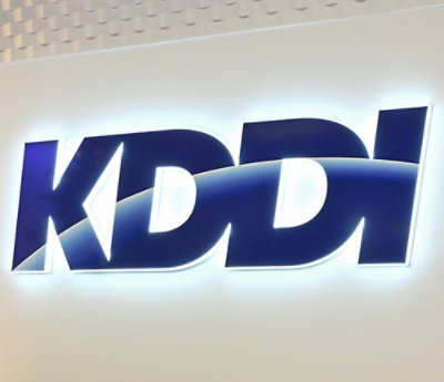Illuminated KDDI sign on white textured background.