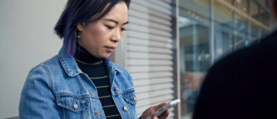 Person with purple hair holding smartphone in indoor setting.