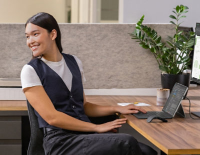 Smiling woman at desk using tablet and monitor for work.