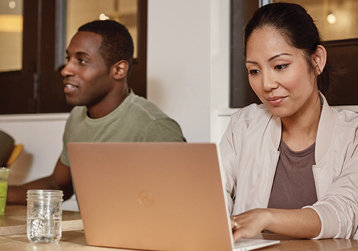 Two people sitting at a conference table, one of them working on a laptop