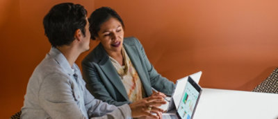 A man and woman sitting at a table looking at a laptop.