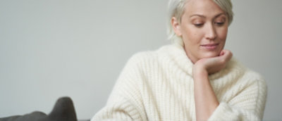 A woman wearing a white sweater with her hand resting on her chin.