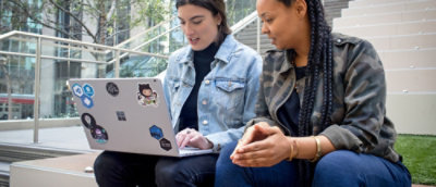 A woman sitting on a bench with a laptop.