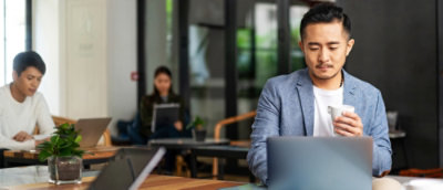 一位穿着西装的男士坐在桌前使用笔记本电脑。