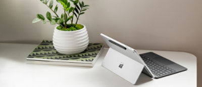 桌上有一台平板电脑，其旁边有一个插着绿叶的白壶。