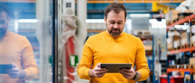 A man wearing yellow t-shirt holding a tab in hands