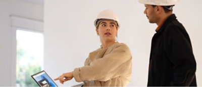 Two individuals in hard hats, one pointing at a laptop screen.