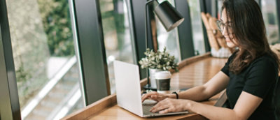 A women typing on a laptop at a wooden desk.