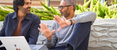 Two men engaged in a casual outdoor discussion with a laptop.