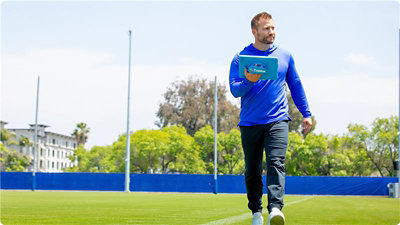 A person holding a Microsoft Surface tablet walking on a football field