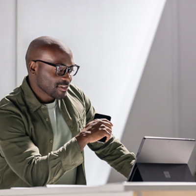 Seorang pria memegang ponsel dengan tangan dan bekerja di depan laptop